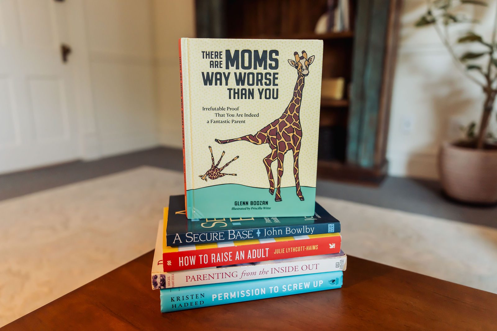 A stack of parenting books on the coffee table, topped by There Are Moms Way Worse Than You
