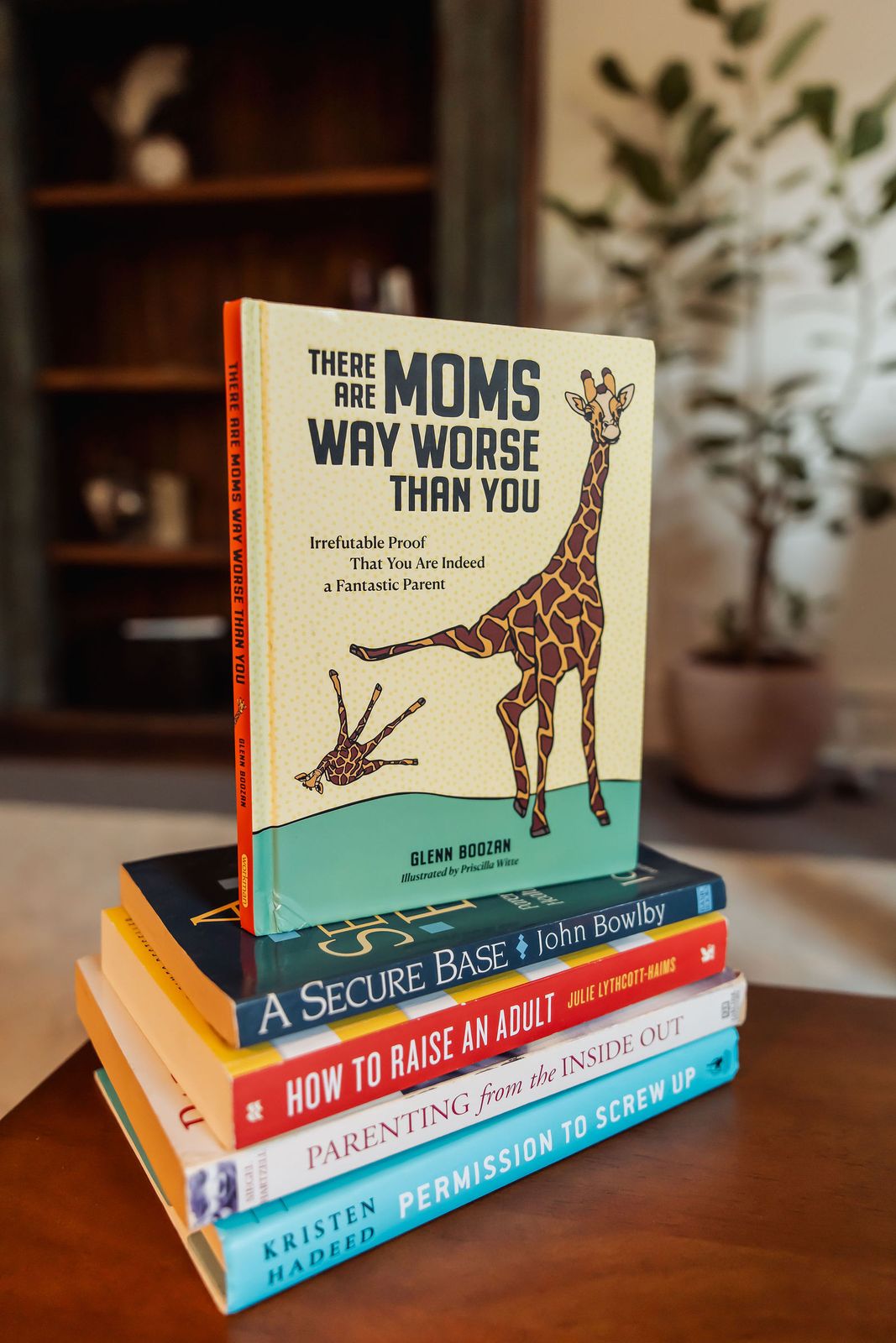 A stack of parenting books on the coffee table, topped by There Are Moms Way Worse Than You